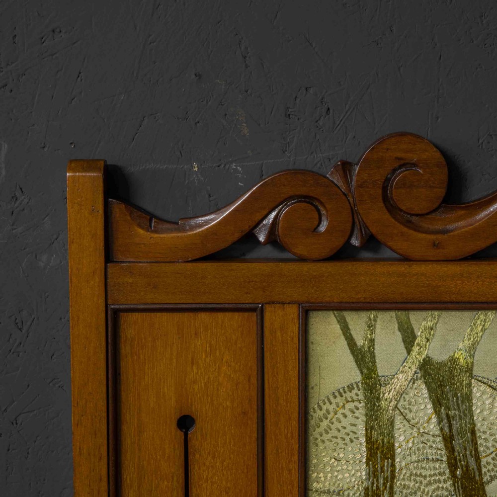 An Edwardian carved mahogany overmantel frame featuring a central embroidered panel depicting a figure with a lion, topped with scrollwork and an inverted heart cutout at the base. View II