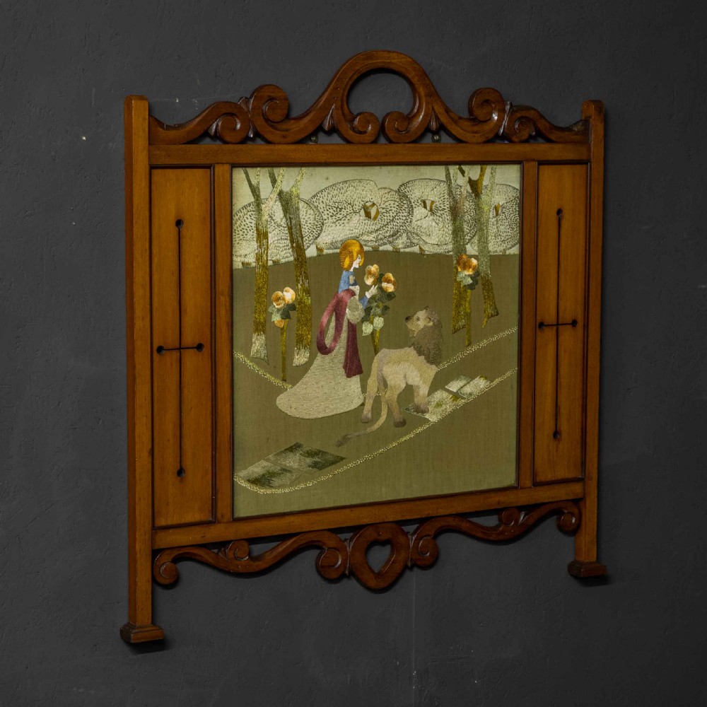 An Edwardian carved mahogany overmantel frame featuring a central embroidered panel depicting a figure with a lion, topped with scrollwork and an inverted heart cutout at the base. View III
