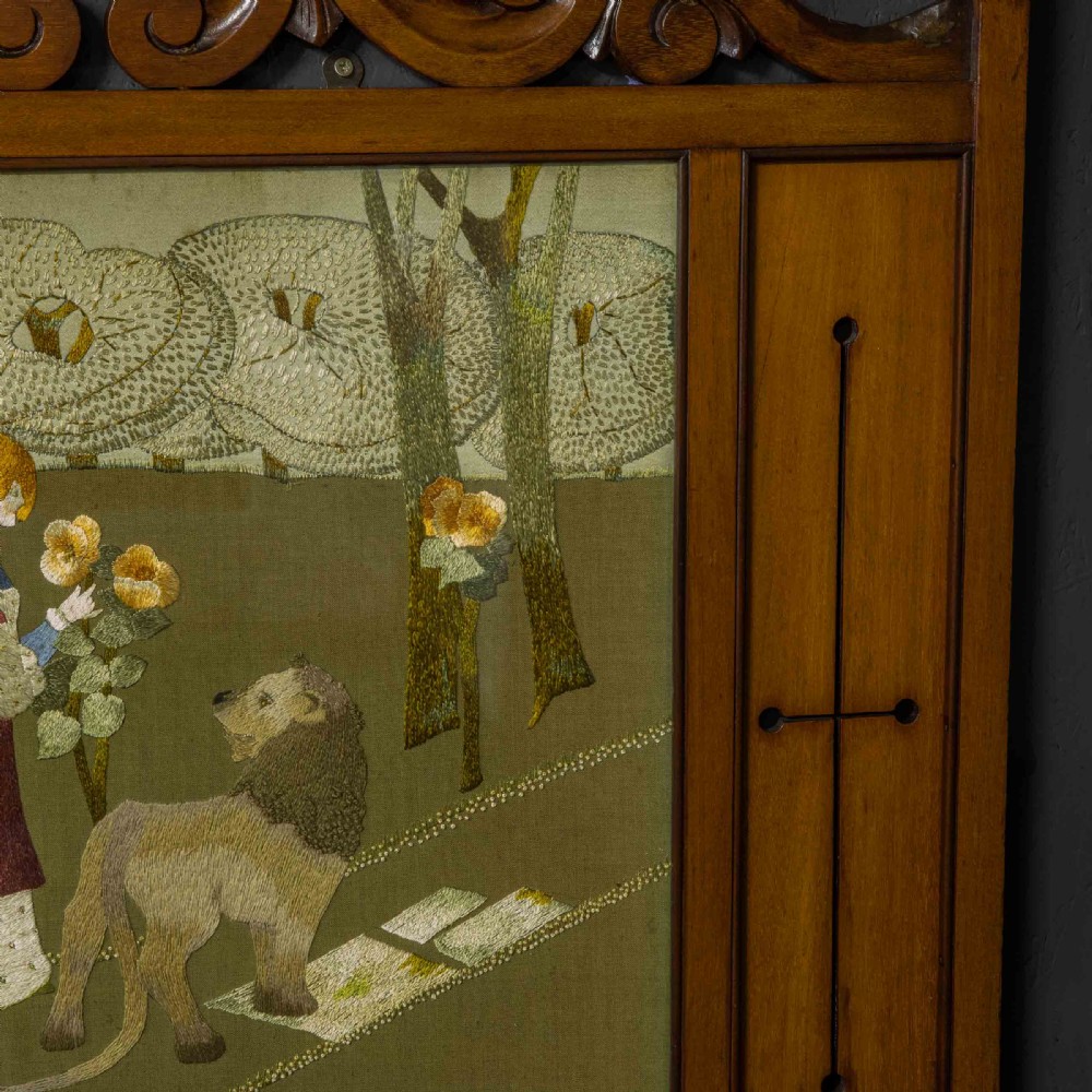An Edwardian carved mahogany overmantel frame featuring a central embroidered panel depicting a figure with a lion, topped with scrollwork and an inverted heart cutout at the base. View V