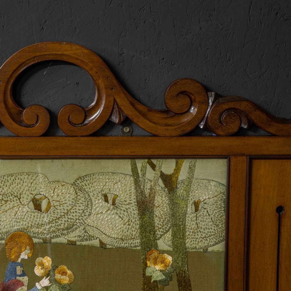 An Edwardian carved mahogany overmantel frame featuring a central embroidered panel depicting a figure with a lion, topped with scrollwork and an inverted heart cutout at the base. View VI