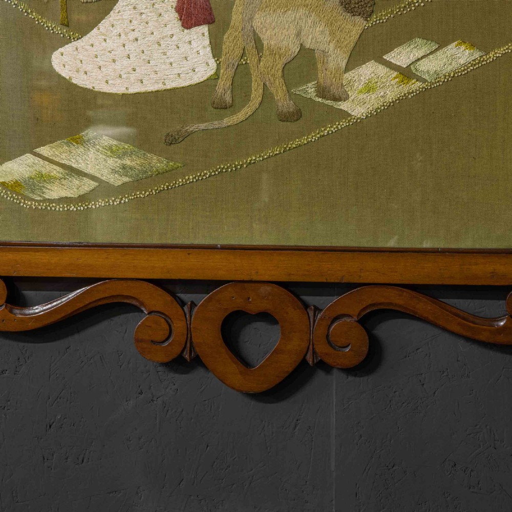 An Edwardian carved mahogany overmantel frame featuring a central embroidered panel depicting a figure with a lion, topped with scrollwork and an inverted heart cutout at the base. View VII
