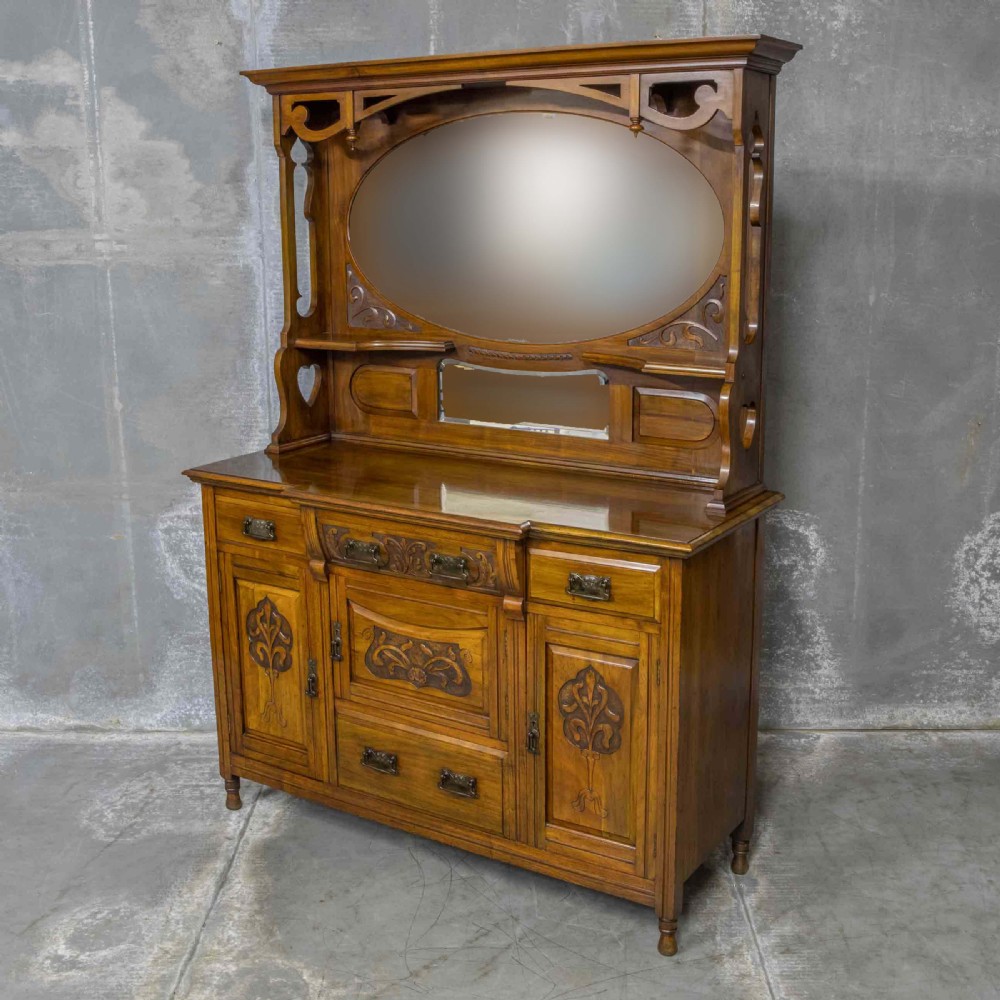 A Victorian walnut sideboard featuring carved panelled cupboard doors, drawers with brass handles, and a mirrored upper shelf structure.