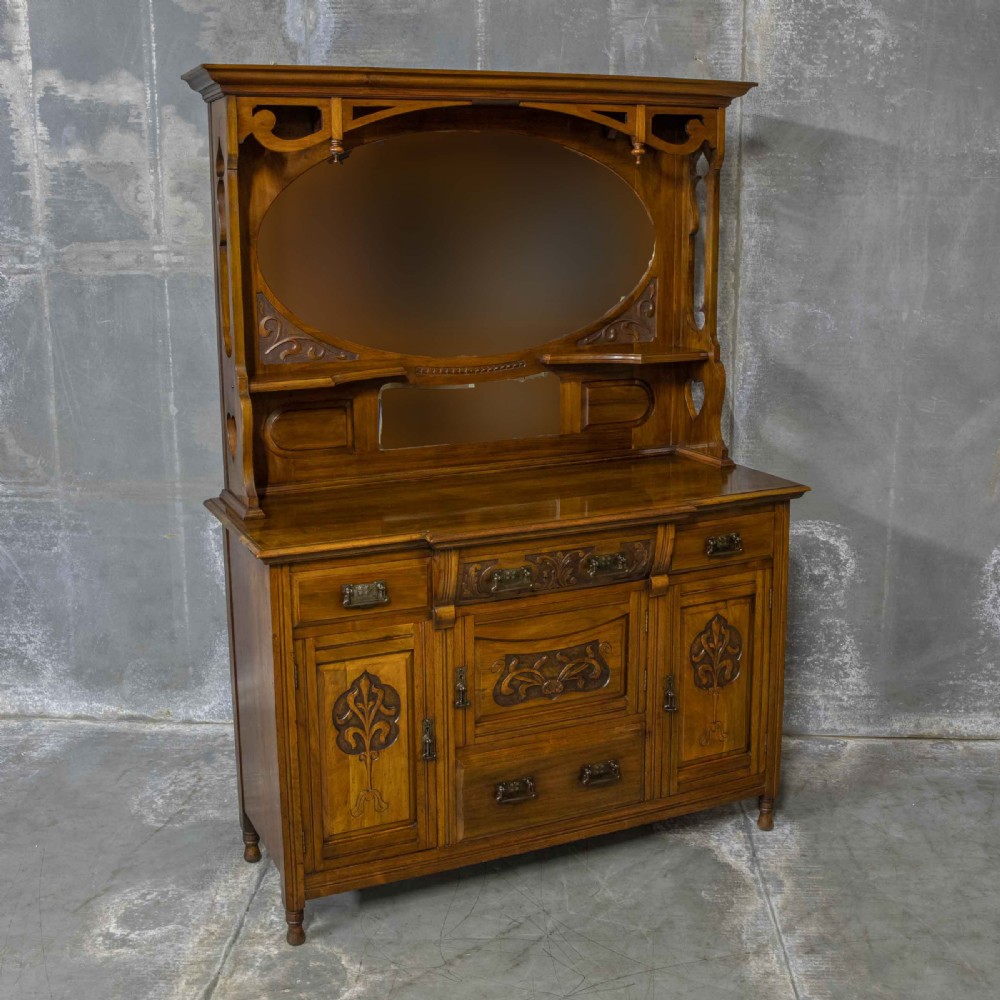 A Victorian walnut sideboard featuring carved panelled cupboard doors, drawers with brass handles, and a mirrored upper shelf structure. View II
