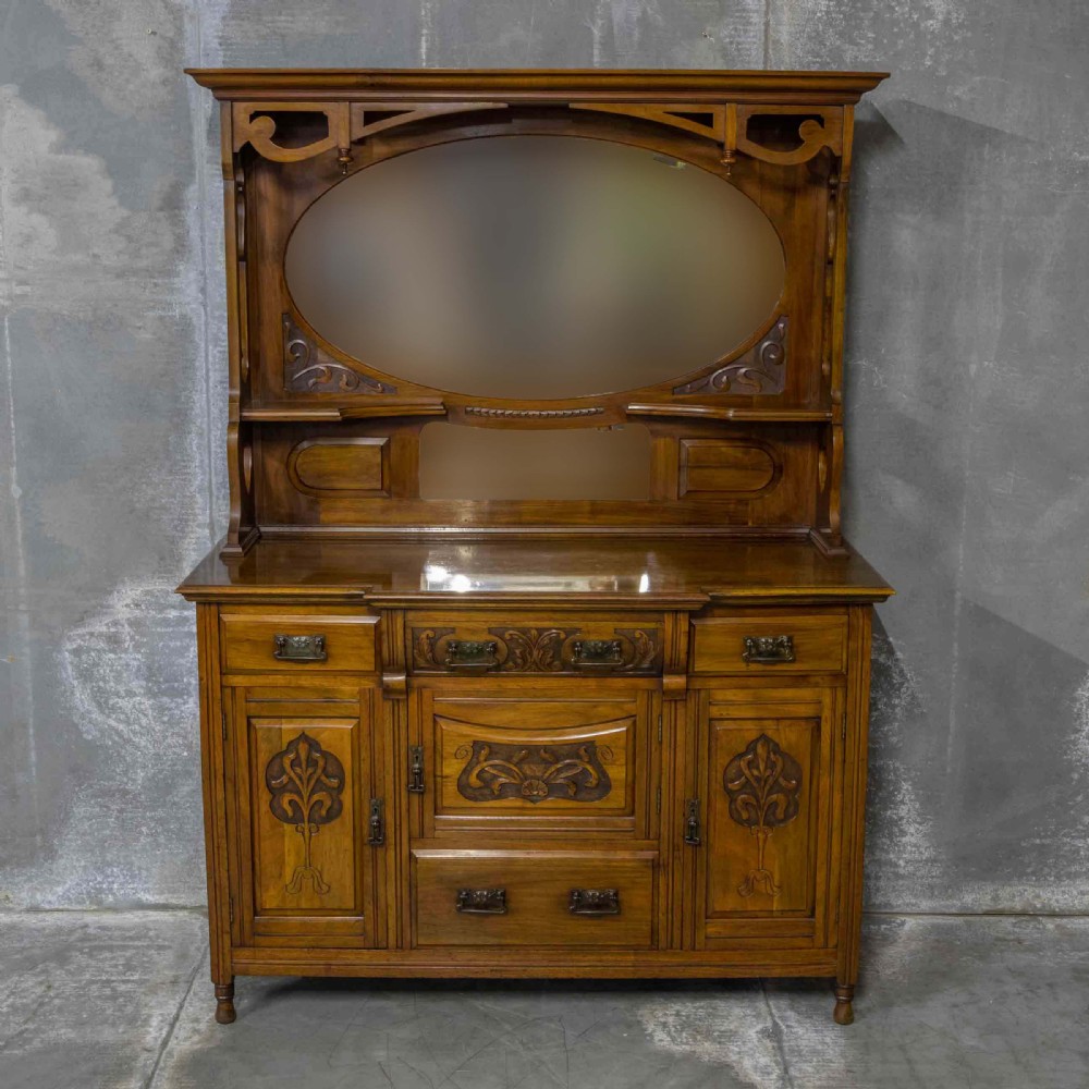A Victorian walnut sideboard featuring carved panelled cupboard doors, drawers with brass handles, and a mirrored upper shelf structure. View III