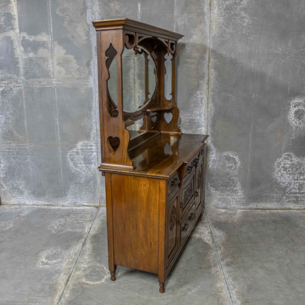 A Victorian walnut sideboard featuring carved panelled cupboard doors, drawers with brass handles, and a mirrored upper shelf structure. View IV