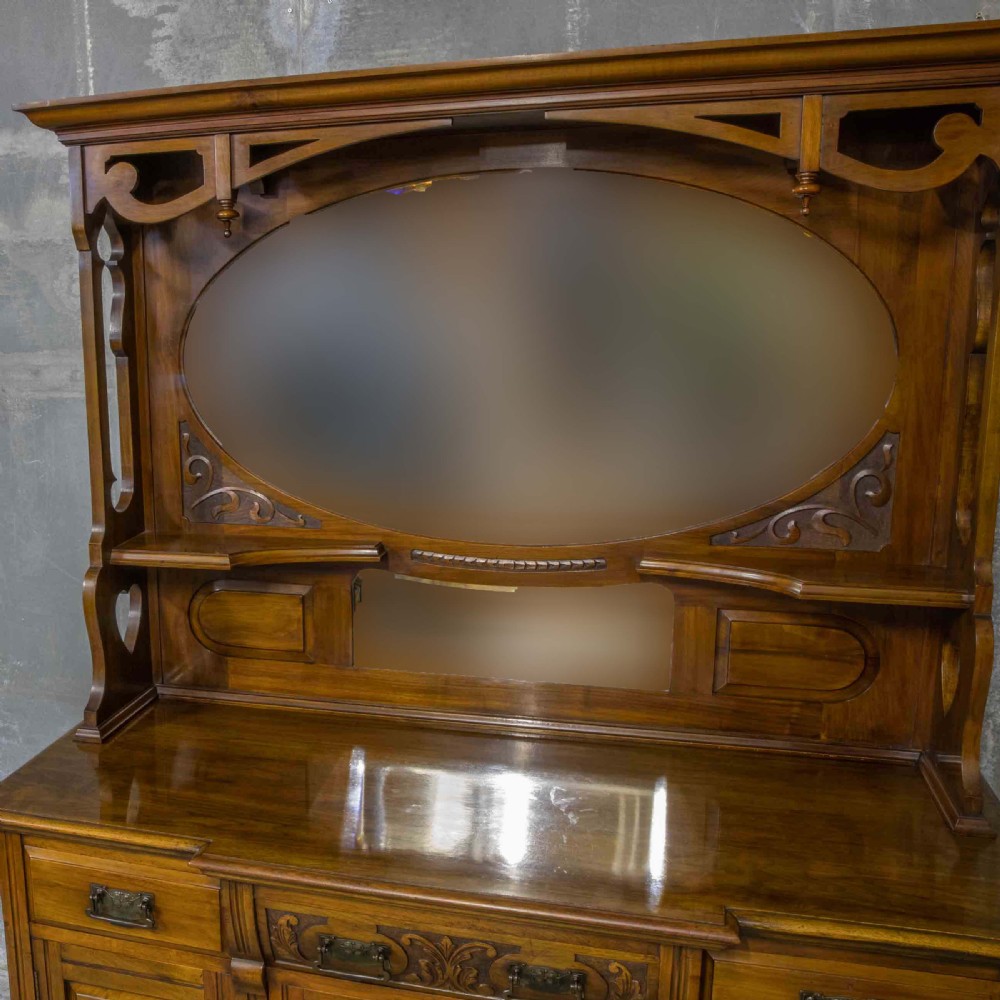 A Victorian walnut sideboard featuring carved panelled cupboard doors, drawers with brass handles, and a mirrored upper shelf structure. View VI
