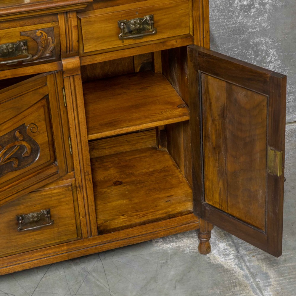 A Victorian walnut sideboard featuring carved panelled cupboard doors, drawers with brass handles, and a mirrored upper shelf structure. View IX