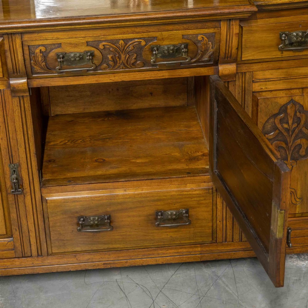 A Victorian walnut sideboard featuring carved panelled cupboard doors, drawers with brass handles, and a mirrored upper shelf structure. View X