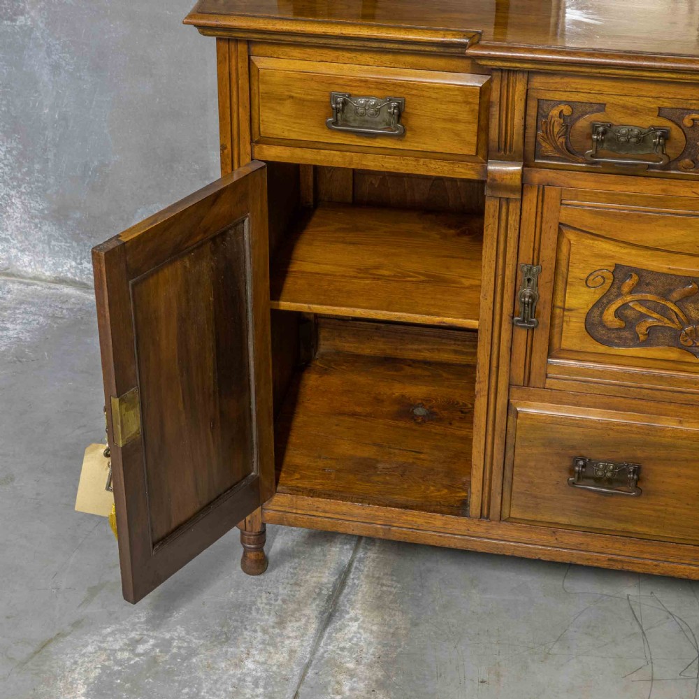 A Victorian walnut sideboard featuring carved panelled cupboard doors, drawers with brass handles, and a mirrored upper shelf structure. View XI