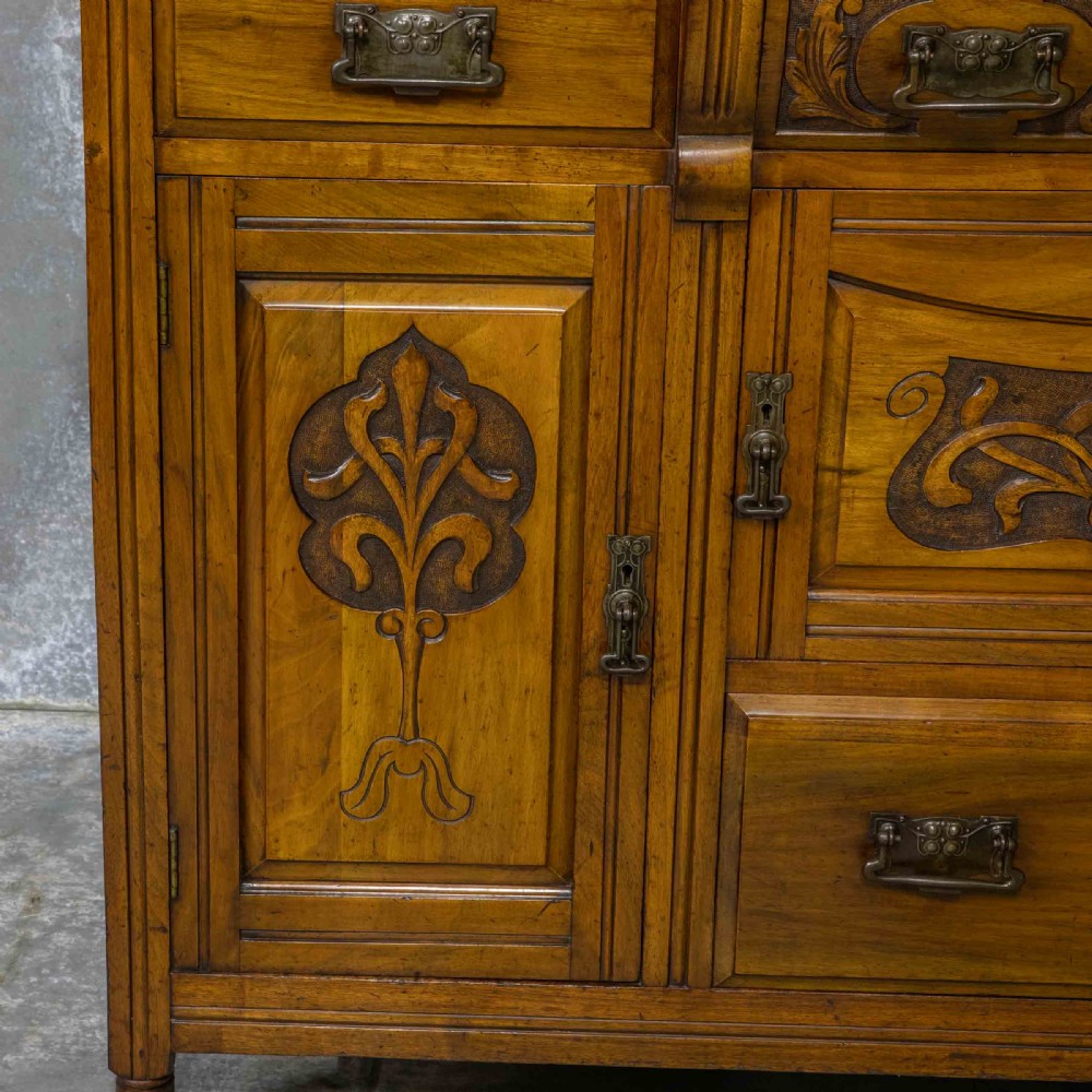 A Victorian walnut sideboard featuring carved panelled cupboard doors, drawers with brass handles, and a mirrored upper shelf structure. View XIII
