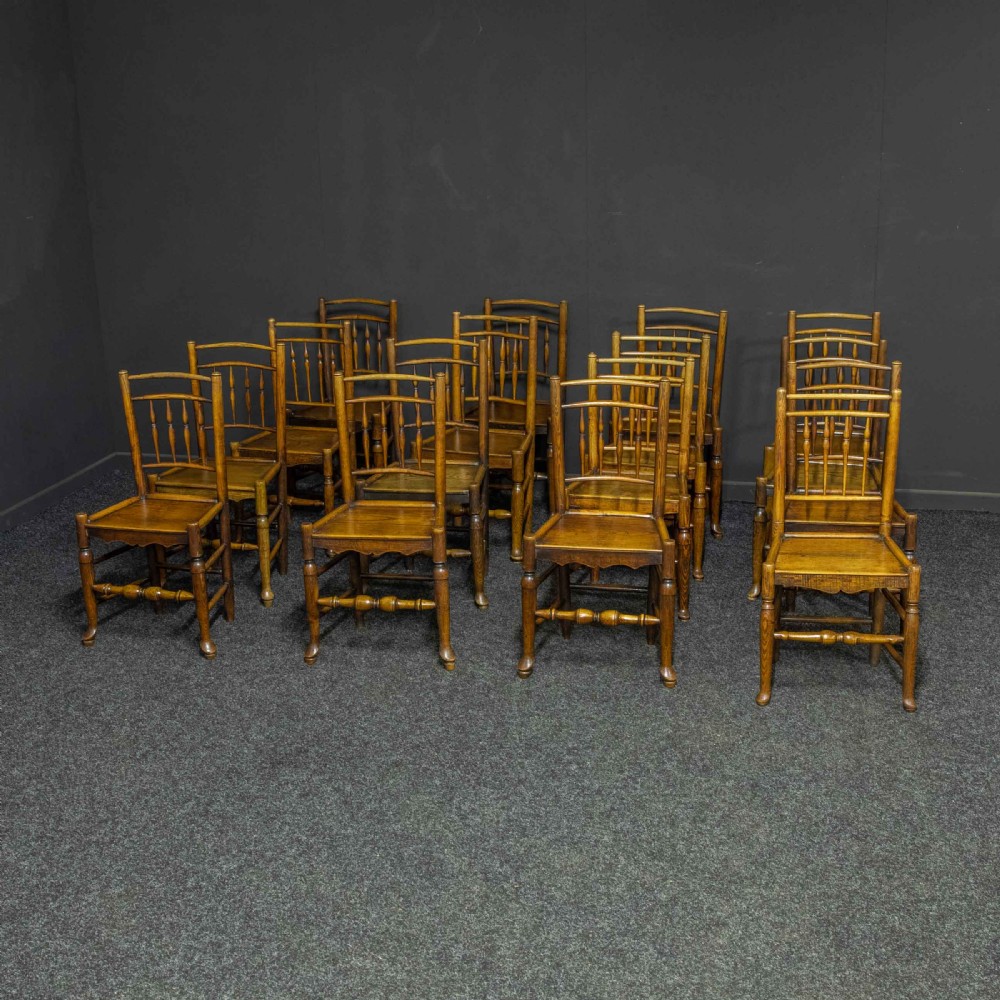 A set of sixteen 18th-century country oak dining chairs featuring spindle backrests, wooden panel seats, turned legs, and stretchers.