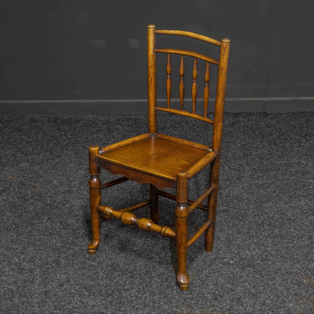 A set of sixteen 18th-century country oak dining chairs featuring spindle backrests, wooden panel seats, turned legs, and stretchers. View IV