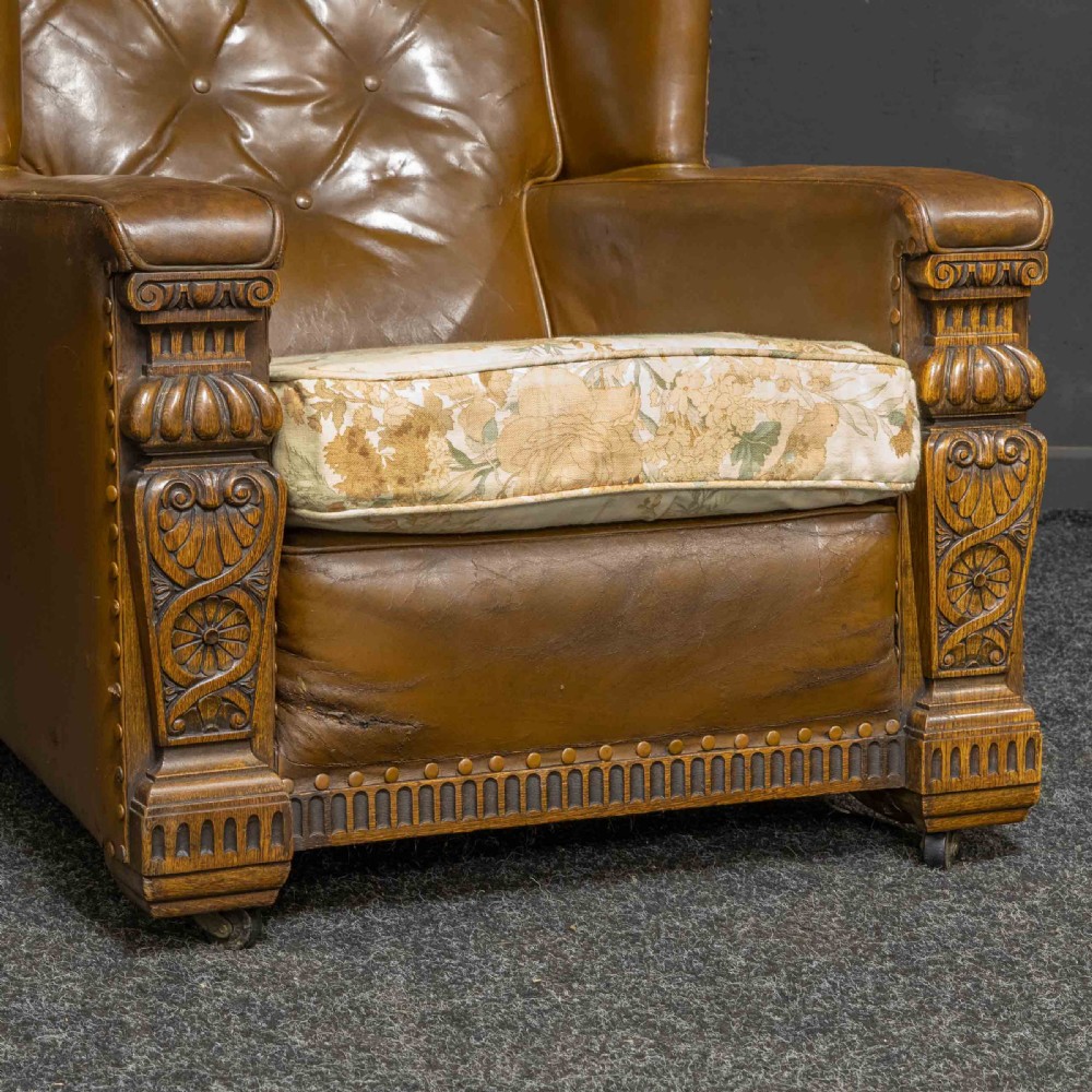 A pair of early 20th-century tan leather armchairs featuring buttoned backs, carved timber front pilasters, and floral patterned fabric seat cushions. View II