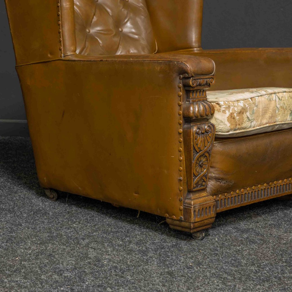 A pair of early 20th-century tan leather armchairs featuring buttoned backs, carved timber front pilasters, and floral patterned fabric seat cushions. View III