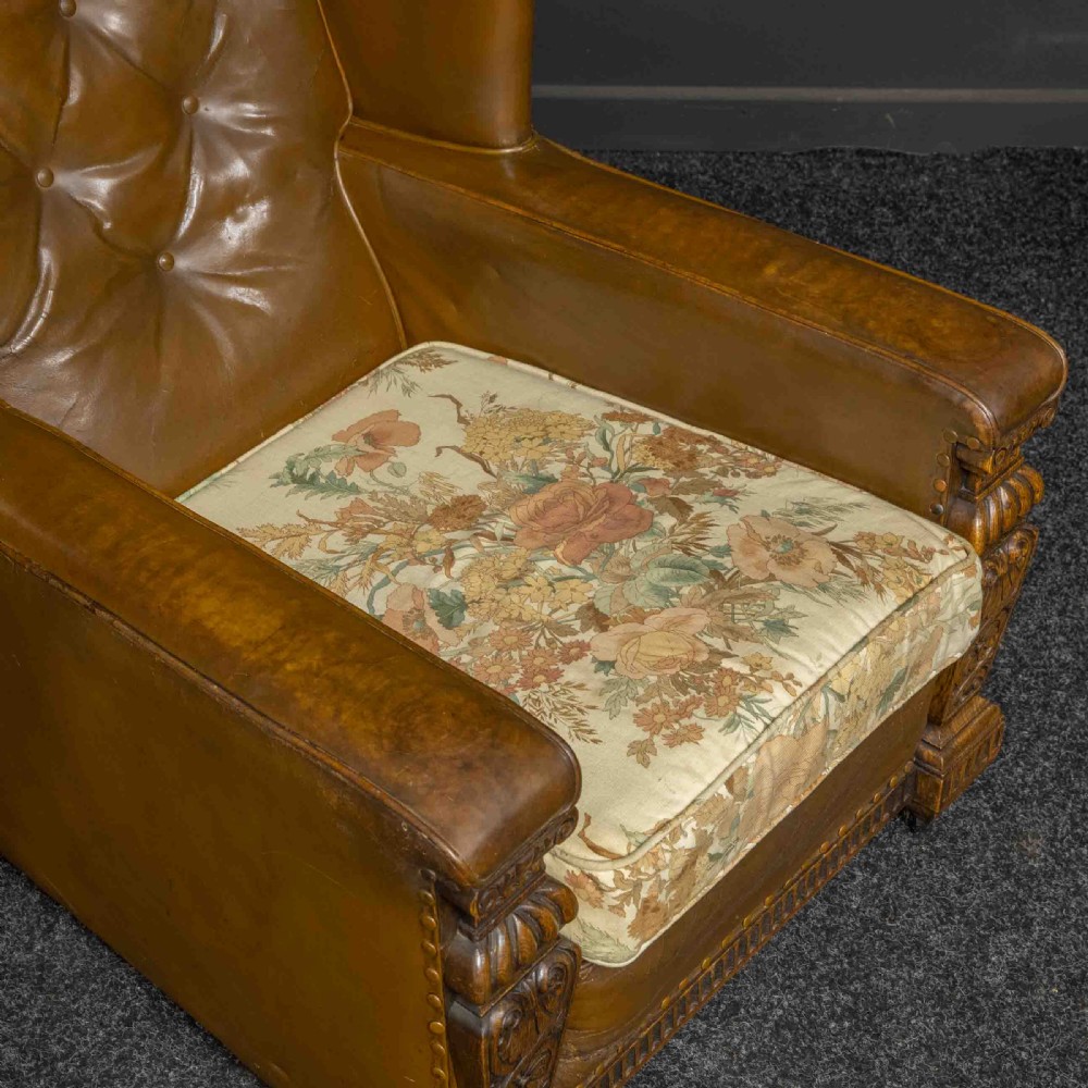 A pair of early 20th-century tan leather armchairs featuring buttoned backs, carved timber front pilasters, and floral patterned fabric seat cushions. View IV