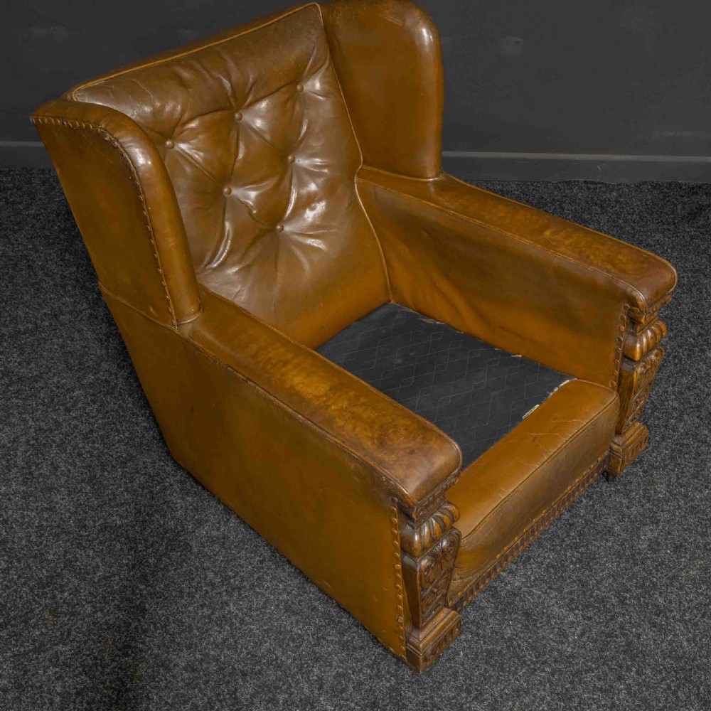 A pair of early 20th-century tan leather armchairs featuring buttoned backs, carved timber front pilasters, and floral patterned fabric seat cushions. View V