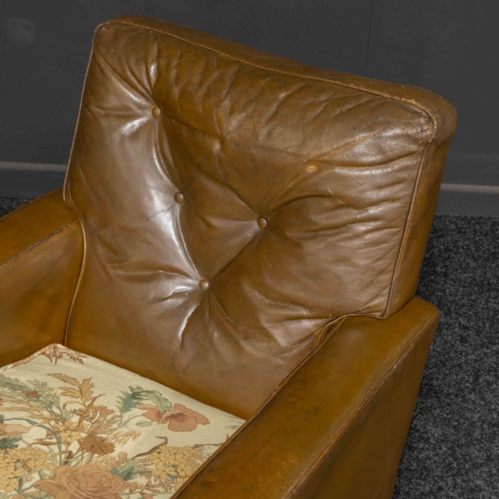 A pair of early 20th-century tan leather armchairs featuring buttoned backs, carved timber front pilasters, and floral patterned fabric seat cushions. View VI