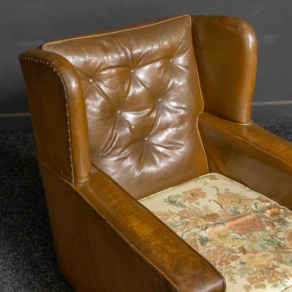A pair of early 20th-century tan leather armchairs featuring buttoned backs, carved timber front pilasters, and floral patterned fabric seat cushions. View VII