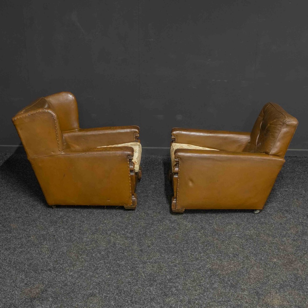 A pair of early 20th-century tan leather armchairs featuring buttoned backs, carved timber front pilasters, and floral patterned fabric seat cushions. View IX
