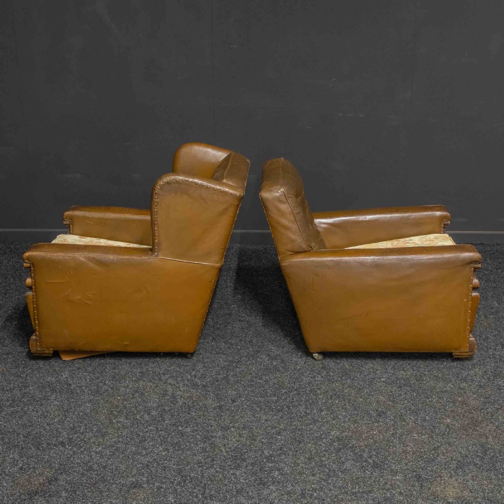 A pair of early 20th-century tan leather armchairs featuring buttoned backs, carved timber front pilasters, and floral patterned fabric seat cushions. View XI