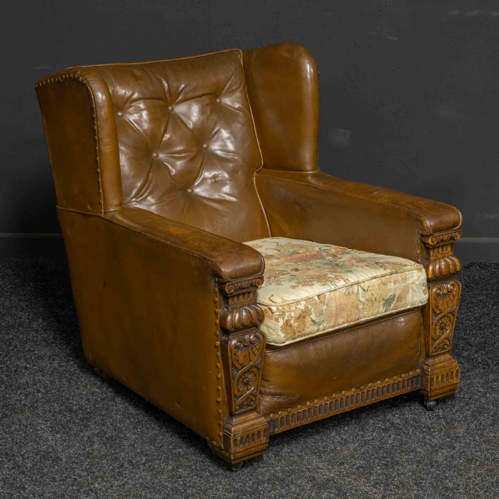 A pair of early 20th-century tan leather armchairs featuring buttoned backs, carved timber front pilasters, and floral patterned fabric seat cushions. View XII