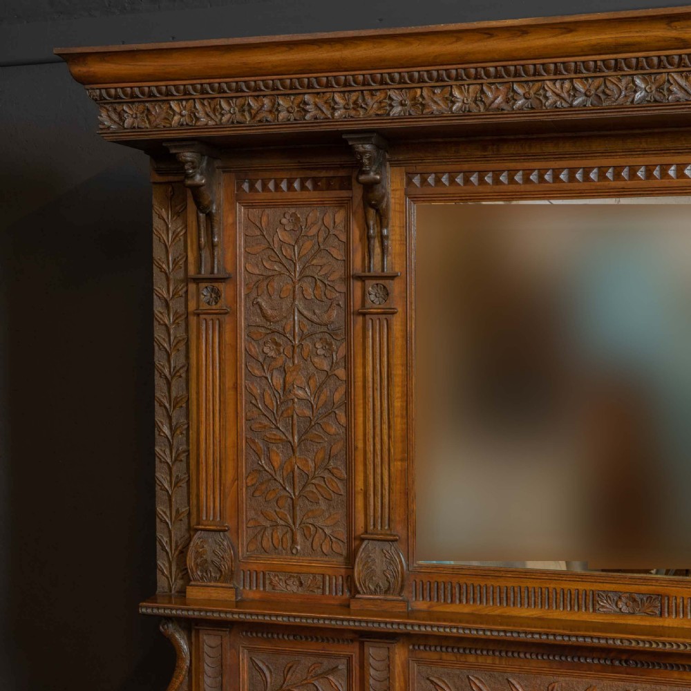 A carved oak Arts and Crafts dresser featuring a mirror back upper section, carved leaf panels, checkerboard inlay counter, and lower cupboards. View VI