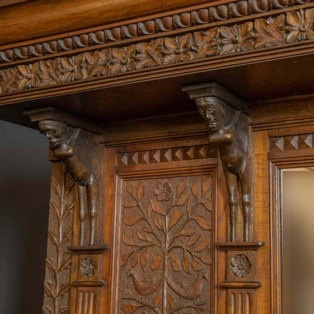A carved oak Arts and Crafts dresser featuring a mirror back upper section, carved leaf panels, checkerboard inlay counter, and lower cupboards. View VII