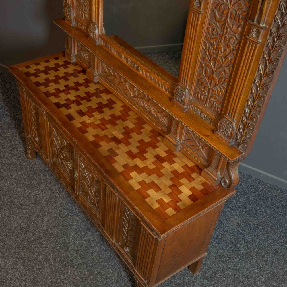 A carved oak Arts and Crafts dresser featuring a mirror back upper section, carved leaf panels, checkerboard inlay counter, and lower cupboards. View XIV