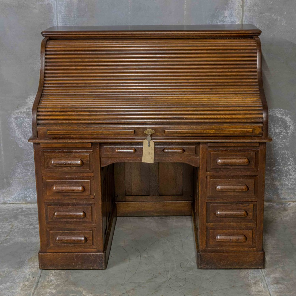 An Edwardian dark oak roll top desk featuring an open slatted tambour hood, fitted interior pigeonhole compartments, and twin pedestals with carved wooden drawer handles. View II
