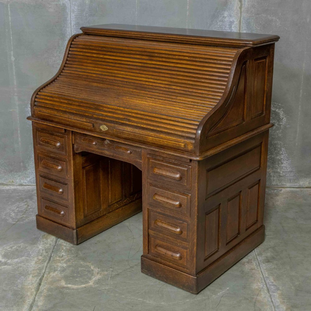 An Edwardian dark oak roll top desk featuring an open slatted tambour hood, fitted interior pigeonhole compartments, and twin pedestals with carved wooden drawer handles. View IV