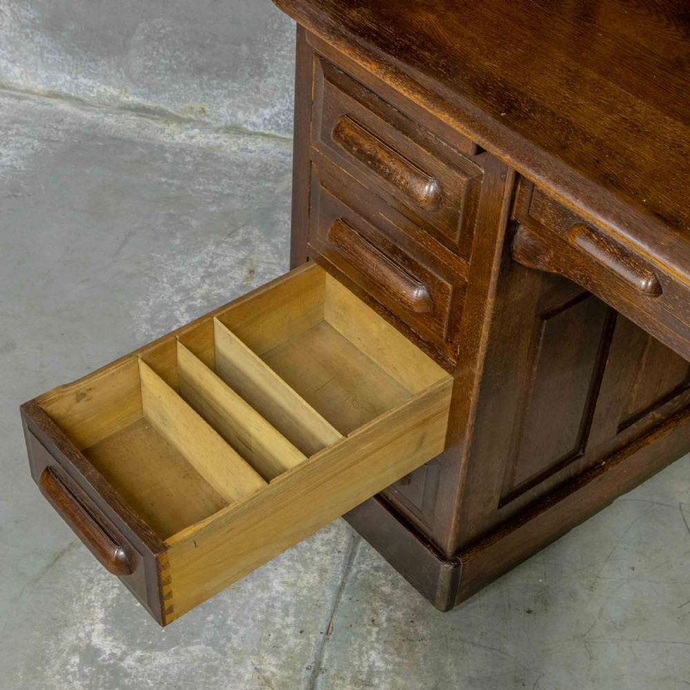 An Edwardian dark oak roll top desk featuring an open slatted tambour hood, fitted interior pigeonhole compartments, and twin pedestals with carved wooden drawer handles. View VI