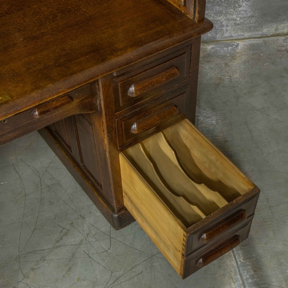 An Edwardian dark oak roll top desk featuring an open slatted tambour hood, fitted interior pigeonhole compartments, and twin pedestals with carved wooden drawer handles. View VII