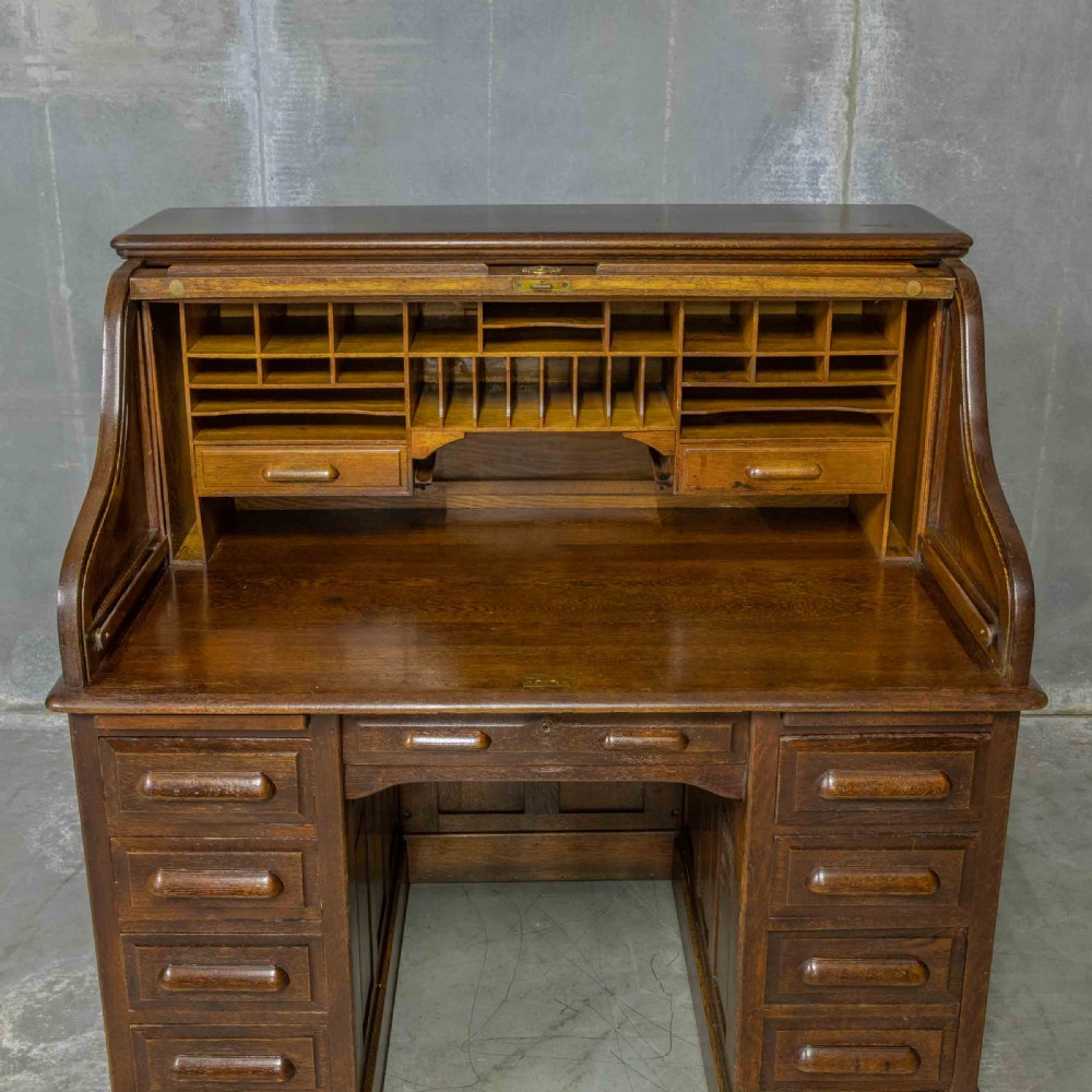 An Edwardian dark oak roll top desk featuring an open slatted tambour hood, fitted interior pigeonhole compartments, and twin pedestals with carved wooden drawer handles. View VIII