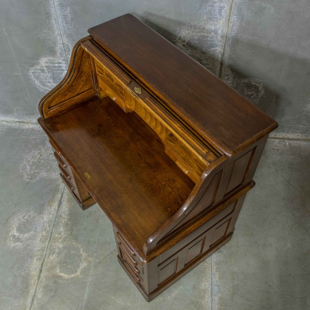 An Edwardian dark oak roll top desk featuring an open slatted tambour hood, fitted interior pigeonhole compartments, and twin pedestals with carved wooden drawer handles. View X