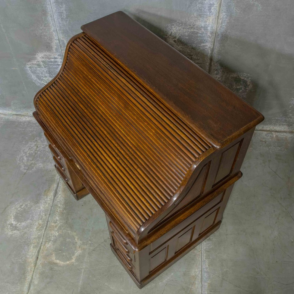 An Edwardian dark oak roll top desk featuring an open slatted tambour hood, fitted interior pigeonhole compartments, and twin pedestals with carved wooden drawer handles. View XI