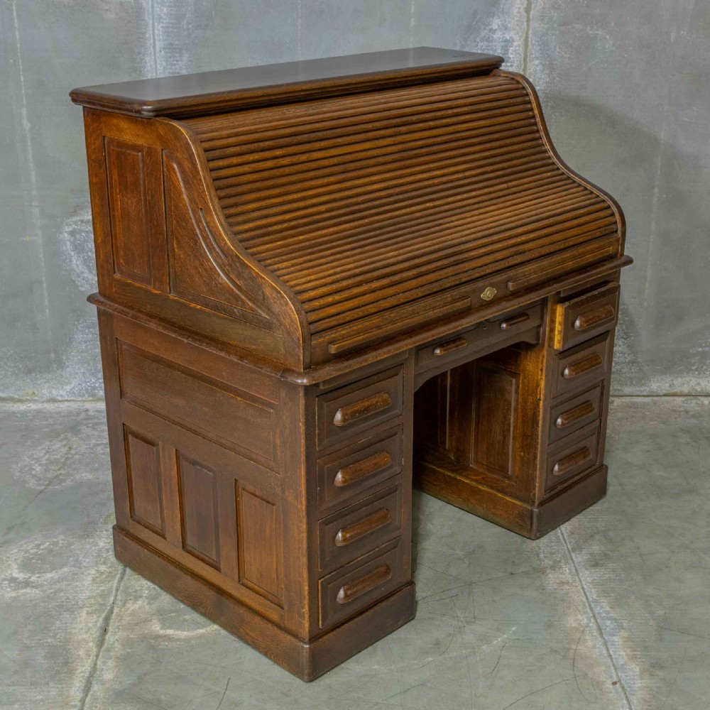 An Edwardian dark oak roll top desk featuring an open slatted tambour hood, fitted interior pigeonhole compartments, and twin pedestals with carved wooden drawer handles. View XIII