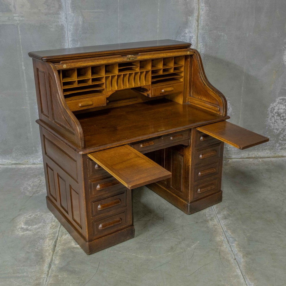 An Edwardian dark oak roll top desk featuring an open slatted tambour hood, fitted interior pigeonhole compartments, and twin pedestals with carved wooden drawer handles. View XIV