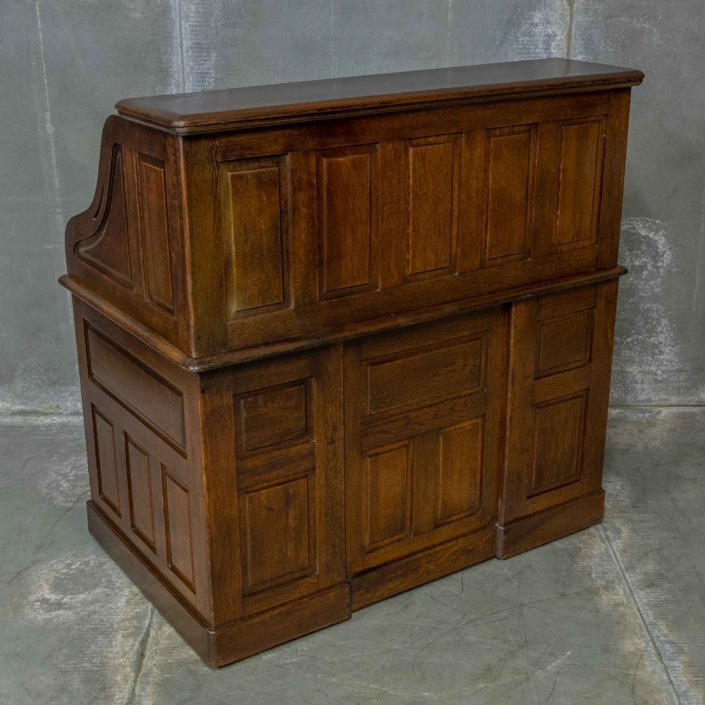 An Edwardian dark oak roll top desk featuring an open slatted tambour hood, fitted interior pigeonhole compartments, and twin pedestals with carved wooden drawer handles. View XVI