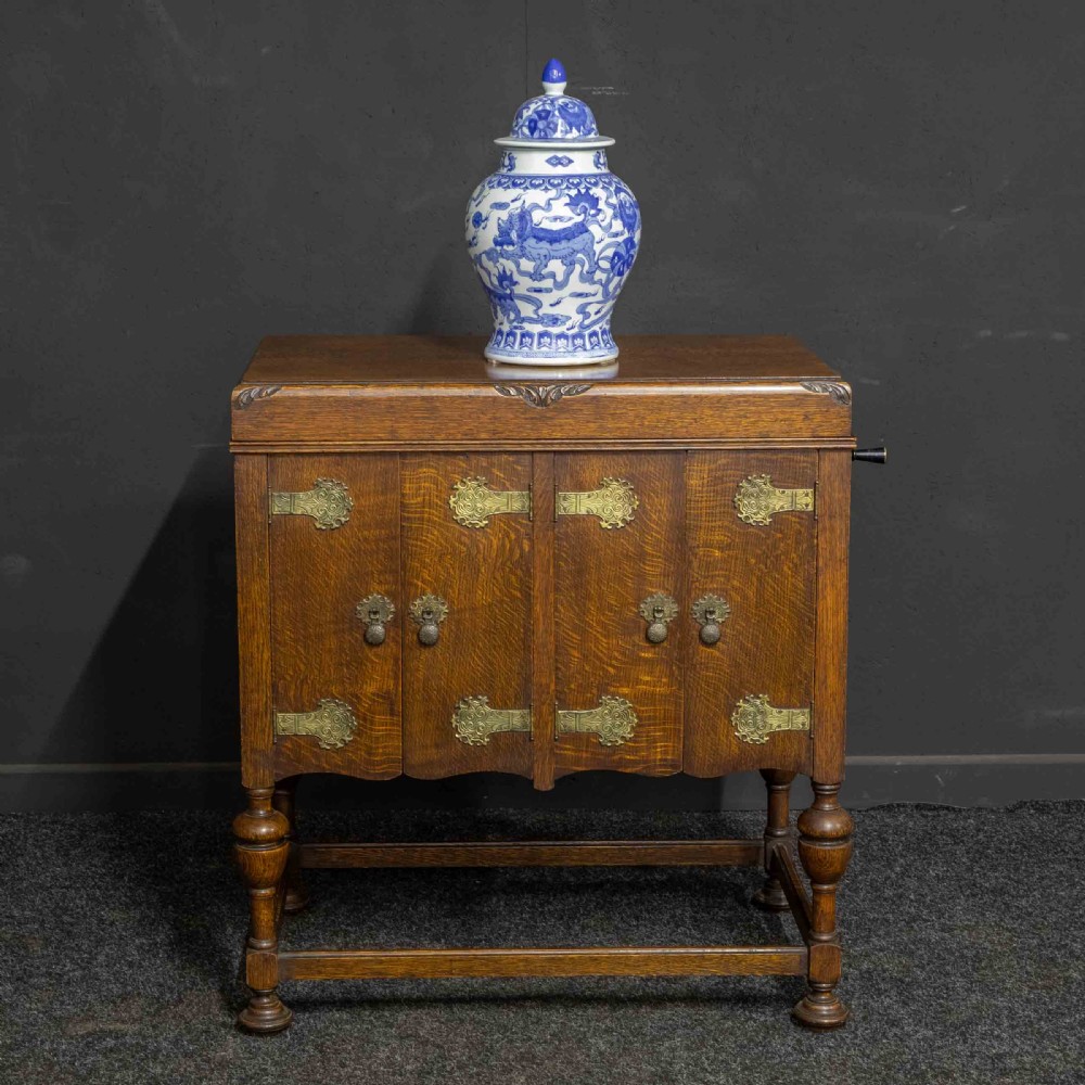 An early 20th-century medium oak wind-up cabinet gramophone with brass strap hinges, drop handles, turned legs, and an open top lid showing the turntable mechanism. View II