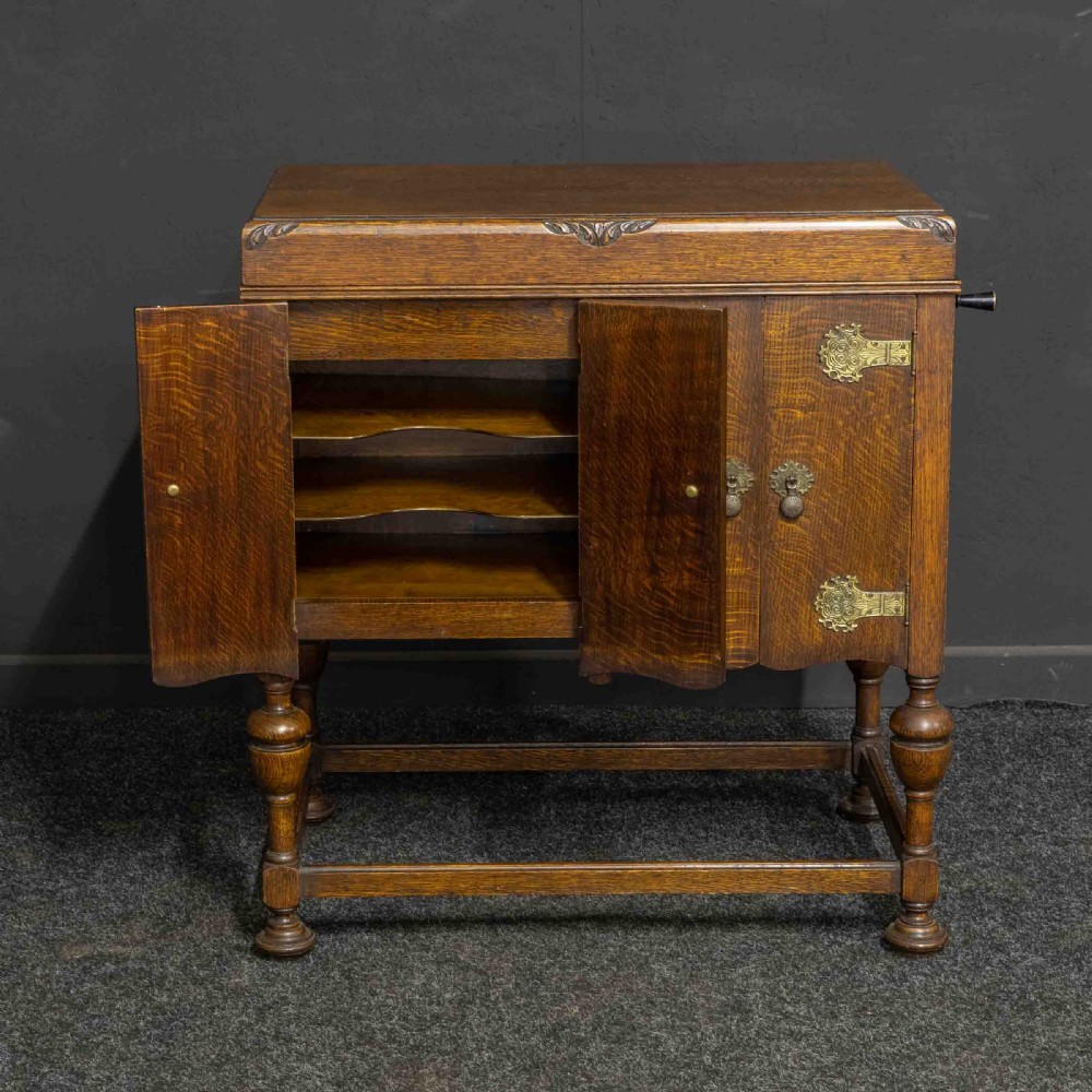 An early 20th-century medium oak wind-up cabinet gramophone with brass strap hinges, drop handles, turned legs, and an open top lid showing the turntable mechanism. View III