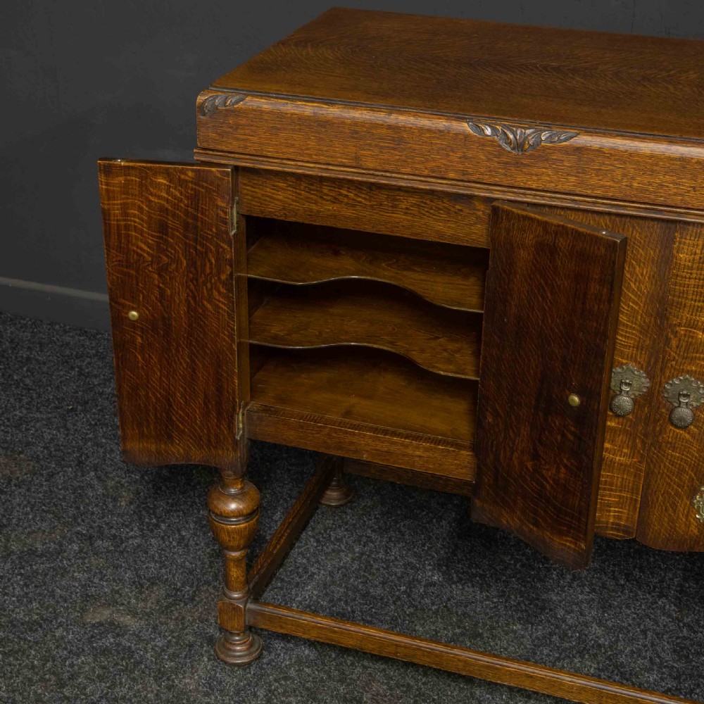 An early 20th-century medium oak wind-up cabinet gramophone with brass strap hinges, drop handles, turned legs, and an open top lid showing the turntable mechanism. View VI