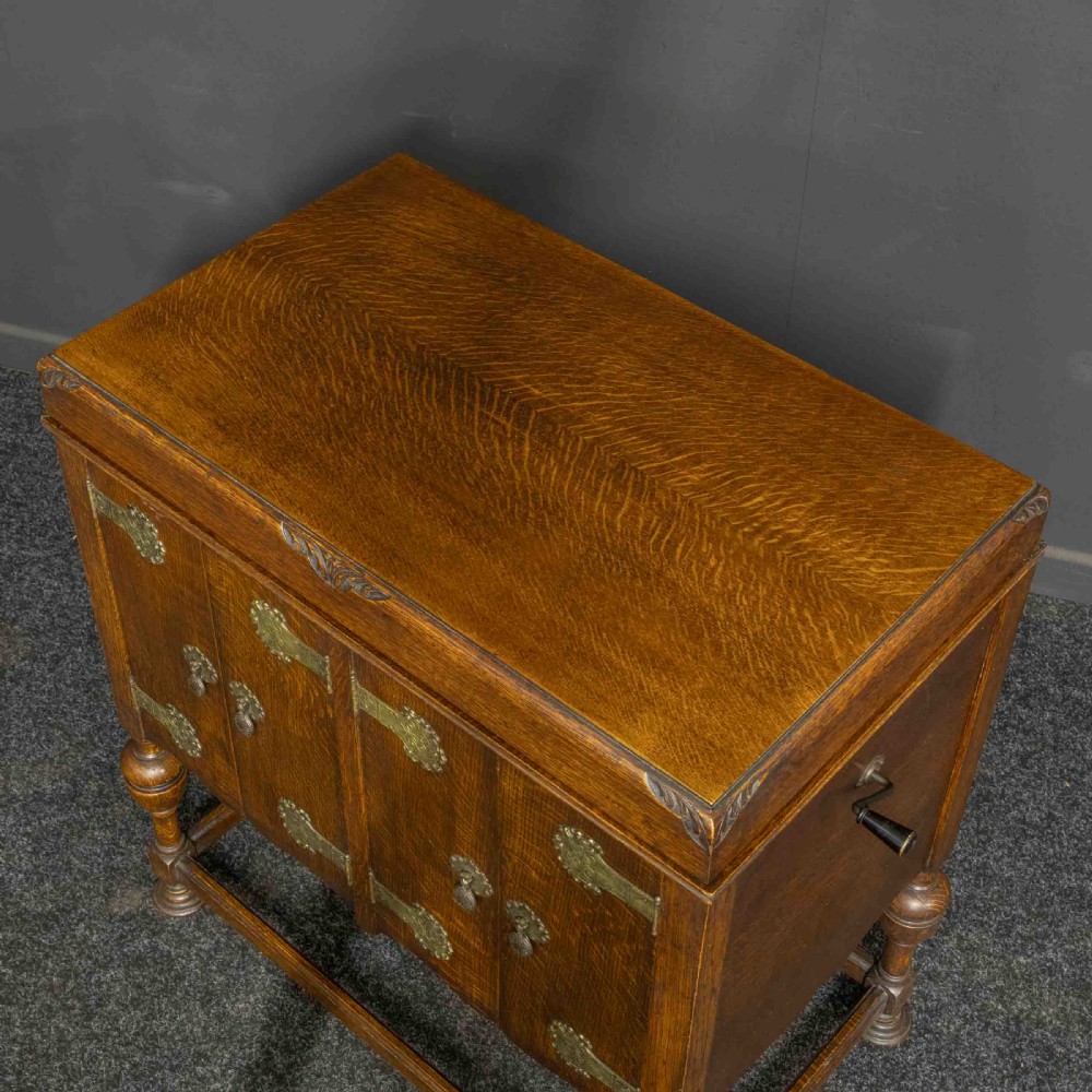 An early 20th-century medium oak wind-up cabinet gramophone with brass strap hinges, drop handles, turned legs, and an open top lid showing the turntable mechanism. View VIII