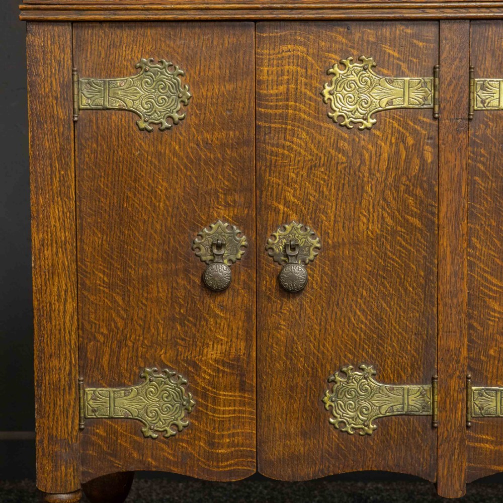An early 20th-century medium oak wind-up cabinet gramophone with brass strap hinges, drop handles, turned legs, and an open top lid showing the turntable mechanism. View XI