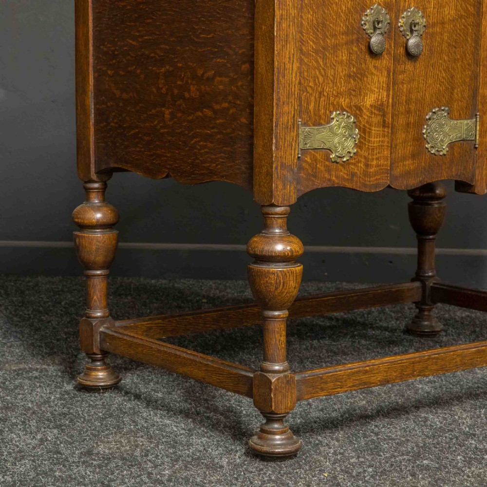 An early 20th-century medium oak wind-up cabinet gramophone with brass strap hinges, drop handles, turned legs, and an open top lid showing the turntable mechanism. View XII