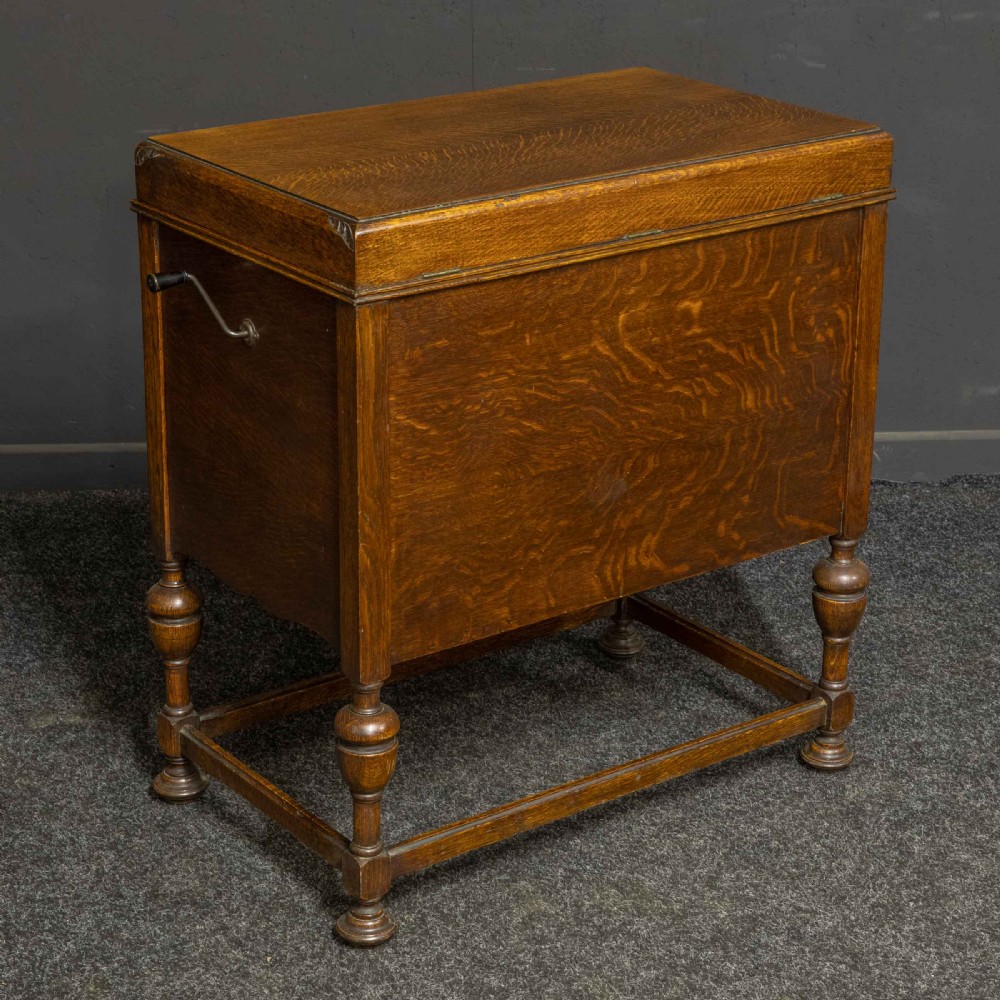 An early 20th-century medium oak wind-up cabinet gramophone with brass strap hinges, drop handles, turned legs, and an open top lid showing the turntable mechanism. View XIV
