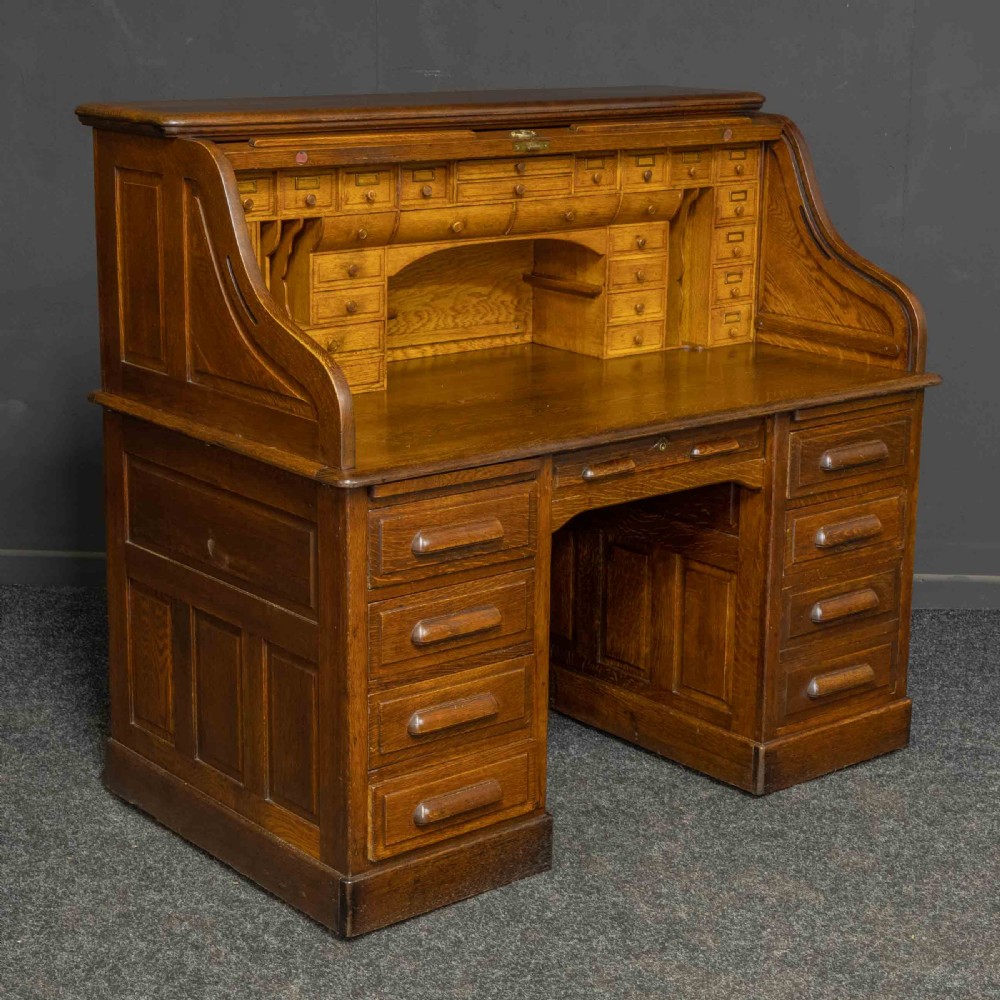 An Edwardian oak roll top desk featuring an S-curve slatted shutter opening to a fitted interior with small drawers and pigeonholes above twin pedestal drawers. View II