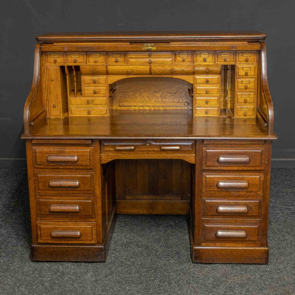 An Edwardian oak roll top desk featuring an S-curve slatted shutter opening to a fitted interior with small drawers and pigeonholes above twin pedestal drawers. View III