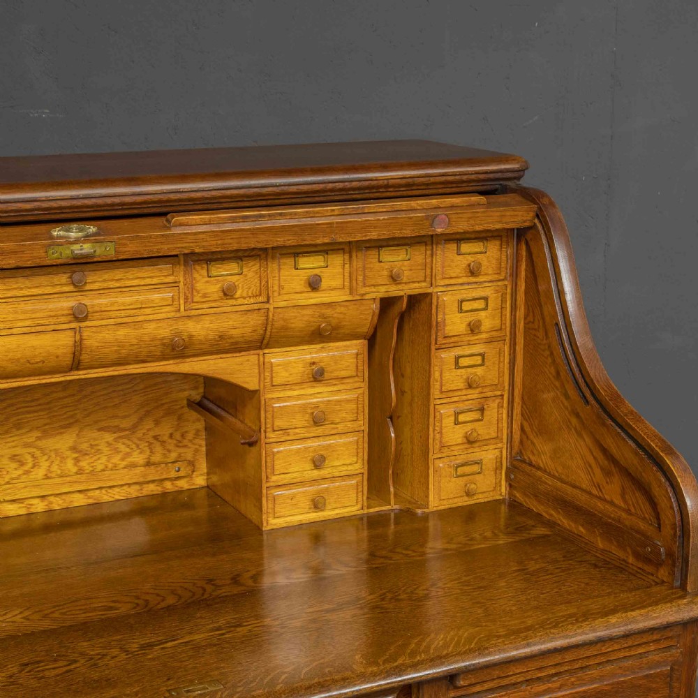 An Edwardian oak roll top desk featuring an S-curve slatted shutter opening to a fitted interior with small drawers and pigeonholes above twin pedestal drawers. View V