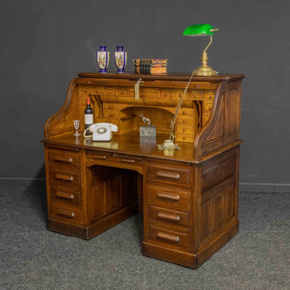 An Edwardian oak roll top desk featuring an S-curve slatted shutter opening to a fitted interior with small drawers and pigeonholes above twin pedestal drawers. View VI