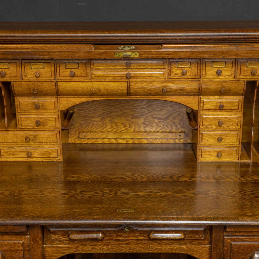 An Edwardian oak roll top desk featuring an S-curve slatted shutter opening to a fitted interior with small drawers and pigeonholes above twin pedestal drawers. View VII